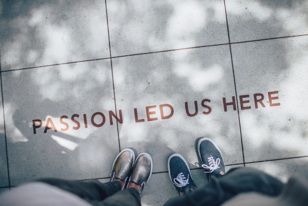 Two person standing on grey floor looking at the quote "Passion led us here" written on the floor. The quote represents how we decide on becoming educators 